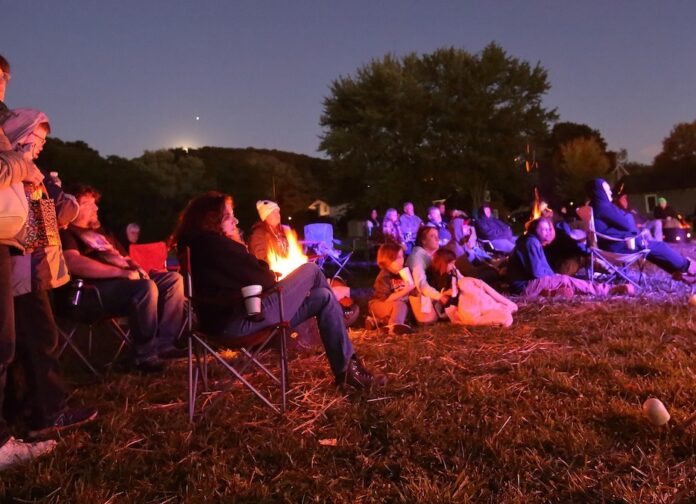 folklore festival people sit in lawn chairs and on the ground, bathed in light from campfires